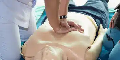 A trainee in scrubs performs cpr on a training dummy during a CPR/AED training course